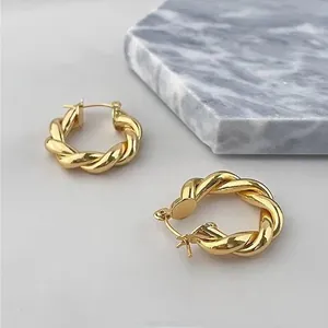 Vue détaillée des boucles d'oreilles créoles torsadées dorées sur fond de marbre minimaliste