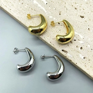 Detailed view of polished gold and silver teardrop stud earrings on stone texture