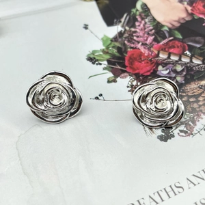 Macro shot of silver rose stud earrings with layered metallic petals on a stone surface