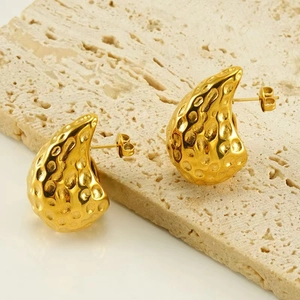 Detailed close-up of golden hammered waterdrop earrings on a natural stone background