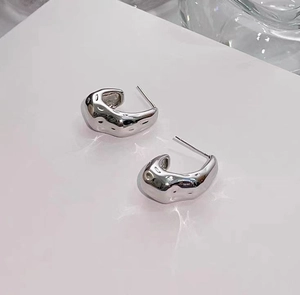 Close-up of chunky silver C-shape earrings with irregular lava textured surface