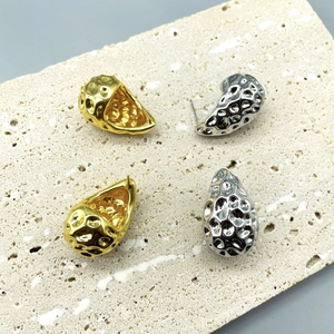 Macro detail of textured gold and silver teardrop earrings on a stone surface