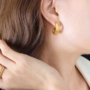 Detail of golden textured strawberry pattern hoop earrings and link ring on a model