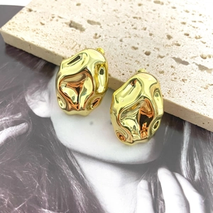 Macro view of gold metal earrings featuring a liquid lava texture and mirror finish