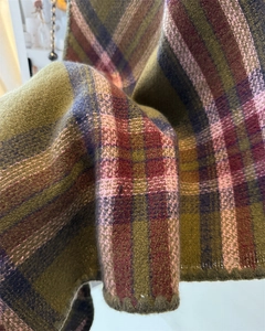 Close-up detail of green and burgundy plaid scarf showing thick woven texture and wavy hem
