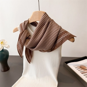 Close-up of brown polka dot silk scarf tied on a white knit sweater with a floral background