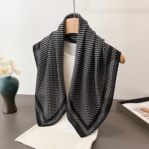 Elegant black and white polka dot silk scarf draped on a wooden hanger over a striped shirt