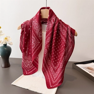 Deep red paisley pattern square scarf hanging on a wooden hanger with elegant accessories