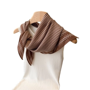 Brown silk scarf with white polka dots tied in a triangle knot on a knit top