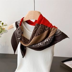 Detail of paisley pattern square silk scarf in orange and brown on a wooden hanger