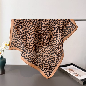 Elegant leopard print cotton linen square scarf in brown and black draped on a metal rack
