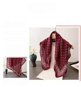 Détail d'un foulard rouge foncé avec des motifs losanges et une texture soyeuse