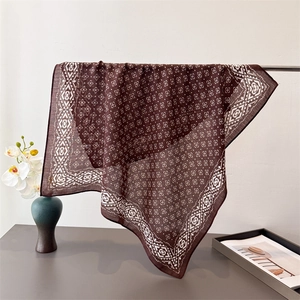 Carré de soie marron avec motif losange géométrique présenté sur un support en métal