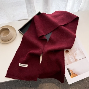 Detailed knit texture of burgundy wool blend scarf with ribbed edges and fabric label