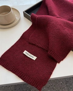 Detail view of burgundy wool blend knit scarf with ribbed edges next to a coffee cup