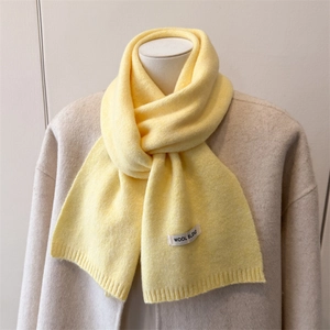 Close-up of soft wool blend knit scarf in light yellow with woven brand label detail