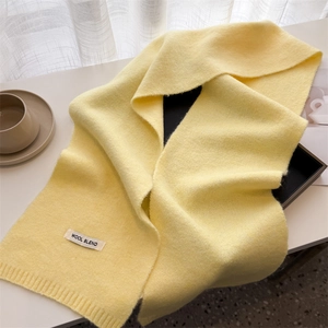 Detail of light yellow wool blend knitted scarf with ribbed edge on a white table