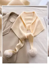 Détail d'une écharpe en maille blanc crème avec pompons doux sur fond de manteau en laine