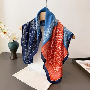 Blue and orange paisley silk scarf draped on a wooden hanger with white knit top