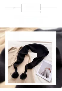 Détail d'une écharpe en maille noire avec pompons sur un manteau beige clair