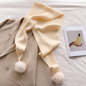 Détail de l'écharpe en tricot crème avec pompons posée sur un manteau en laine