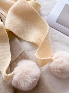 Gros plan d'une écharpe en maille crème avec pompons en peluche sur un manteau en laine