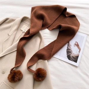 Détail d'une écharpe en maille marron avec pompons sur un fond de manteau blanc