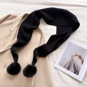 Détail d'une écharpe en maille noire avec pompons sur un manteau en laine beige