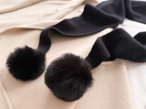 Détail d'une écharpe en maille noire avec pompon en fausse fourrure et texture côtelée