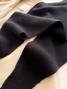 Détail d'une écharpe en maille noire avec texture fine sur un manteau en laine beige chaud