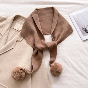 Détail d'une écharpe en maille marron avec pompons sur un manteau en laine beige