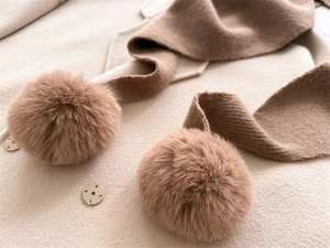 Détail d'une écharpe en maille marron avec pompons en fourrure sur manteau beige