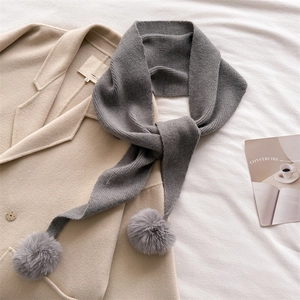 Écharpe en maille grise avec pompons en fourrure sur un manteau beige, look d'hiver