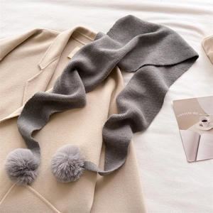 Détail d'une écharpe en tricot gris avec pompons en fourrure sur un manteau de laine beige