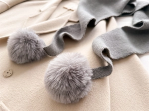 Gros plan détaillé d'une écharpe en maille grise avec pompons en fourrure sur manteau
