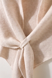 Detalle de chal de punto beige con textura suave y diseño elegante de nudo cruzado