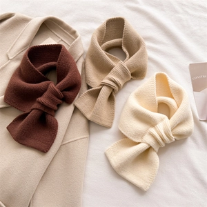 Three knitted crossover scarves in dark brown, khaki, and cream on a wool coat background