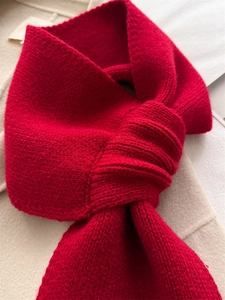Close-up of red knit scarf showing fine texture and cross knot detail on beige fabric