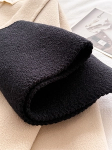 Detailed view of heavy knit texture on a black winter scarf paired with a wool coat