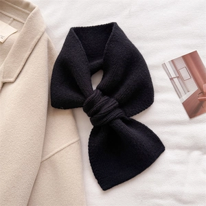 Detailed view of black knitted cross-neck scarf with ribbed texture on a beige coat