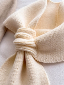 Close-up of cream knit scarf showing soft ribbed texture and elegant bow knot detail