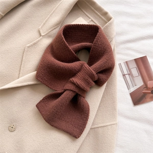 Detailed texture of thick dark brown knitted scarf with a crossover design on a wool coat