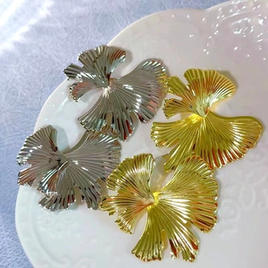 Macro detail of 18K gold and silver ginkgo leaf earrings on white porcelain