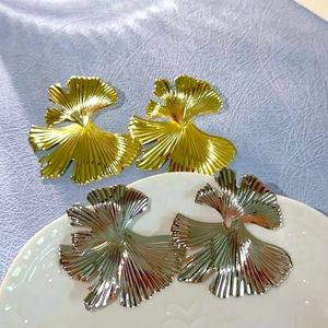 Macro detail of gold and silver ginkgo leaf earrings with radial textured metal finish