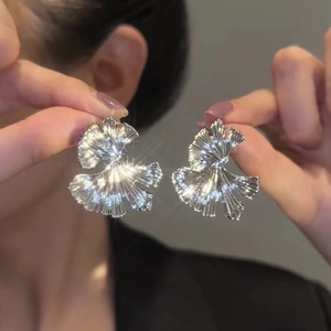 Detailed view of silver ginkgo leaf earrings with radial fold texture on hand