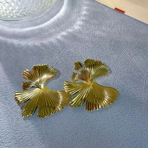 Detailed close-up of 18K gold ginkgo leaf earrings with fine texture on blue fabric
