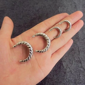 Detailed view of silver twisted C-shaped hoop earrings in two sizes on textured background