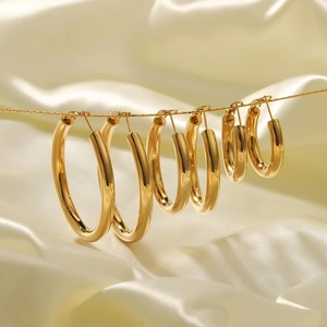 Five pairs of 18K gold plated hoop earrings in various sizes on cream silk backdrop
