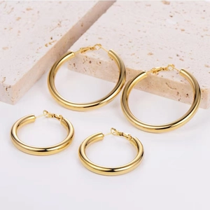 Close-up of chunky gold hoop earrings in two sizes set against a textured stone background