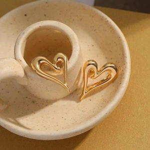 Polished 18K gold-plated irregular heart stud earrings on a ceramic cup edge